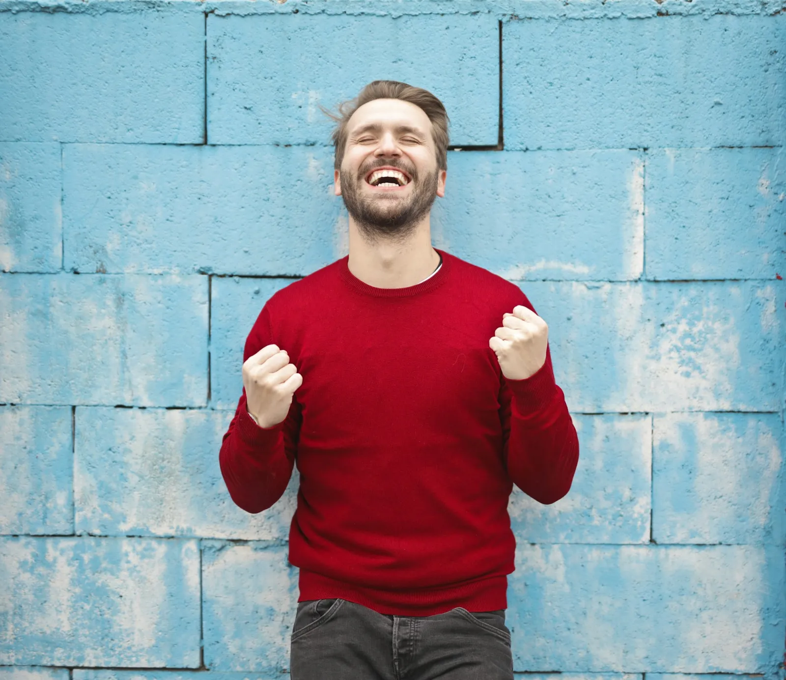 Young man laughing with clenched fists in celebration against a brand-blue painted wall