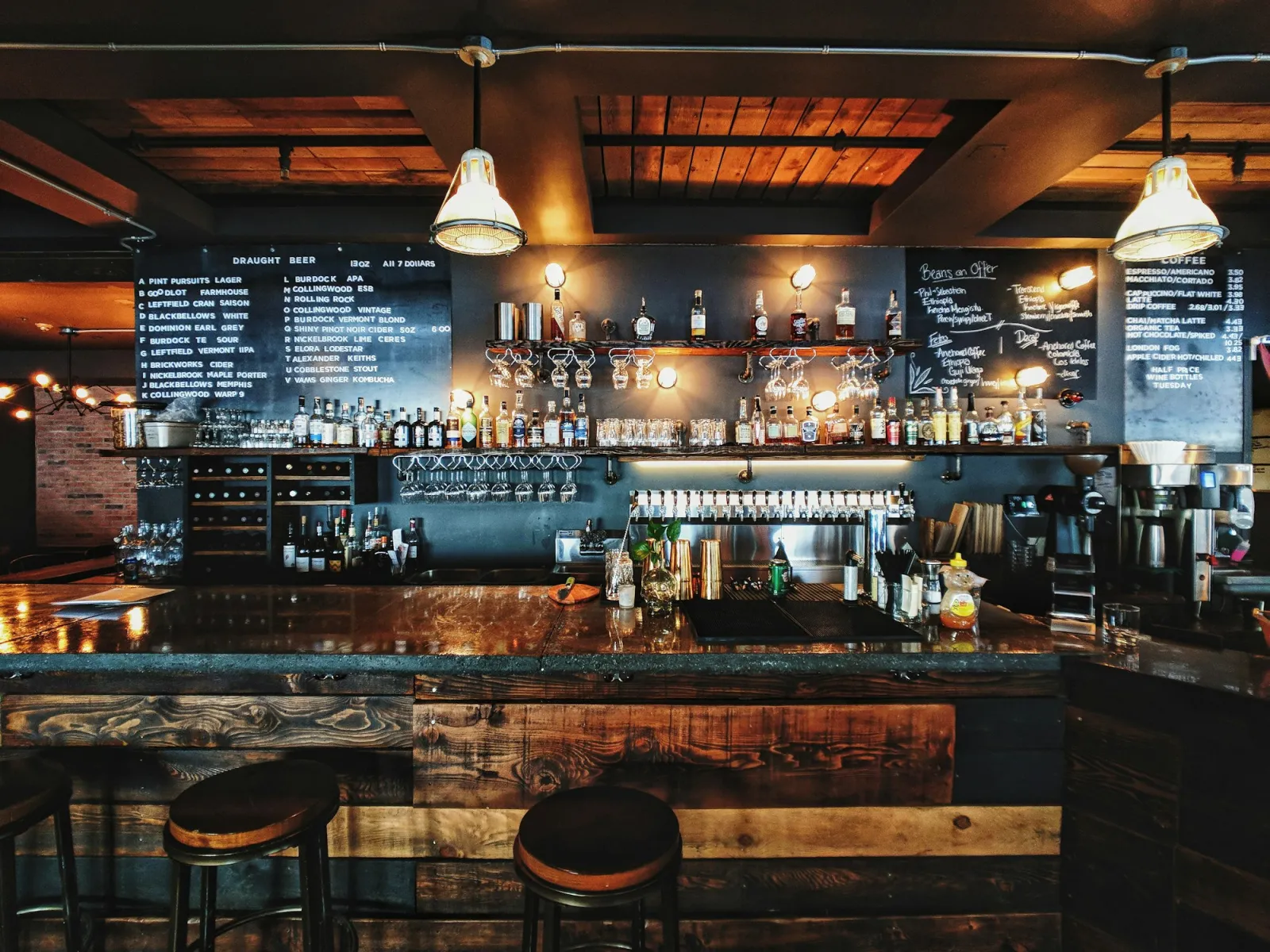 Warm, dimly lit bar interior at night with backlit bottle shelves, a reclaimed-wood counter and stools