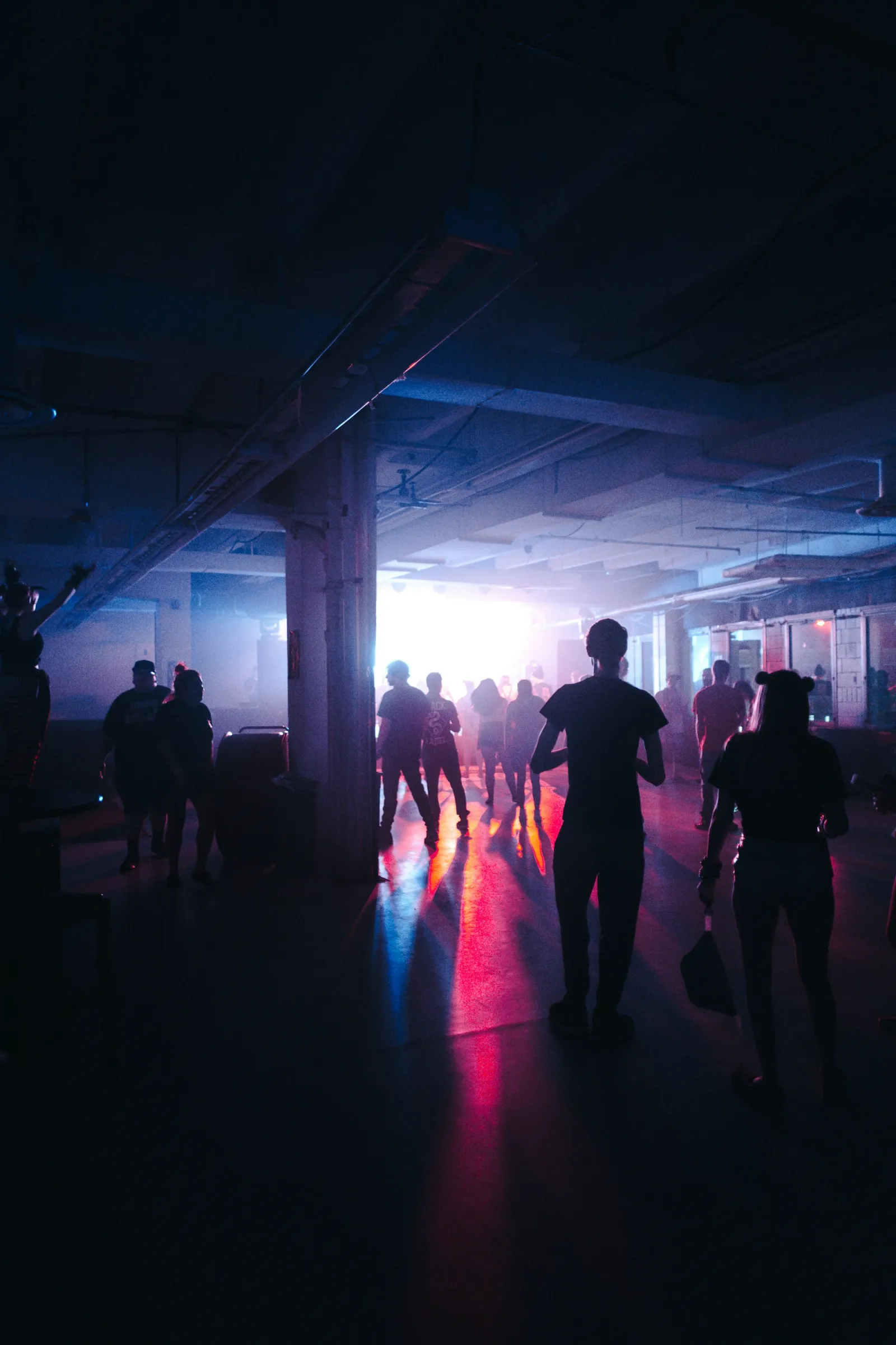 Silhouetted crowd inside a dark entertainment venue lit by a burst of pink and blue stage light